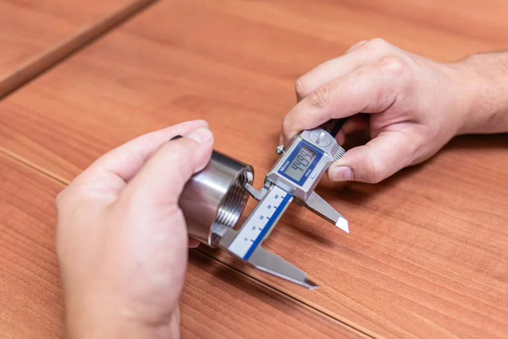 Merjenje kovinskega dela z digitalnim pomičnim merilom za zagotavljanje natančnosti pri proizvodnji.