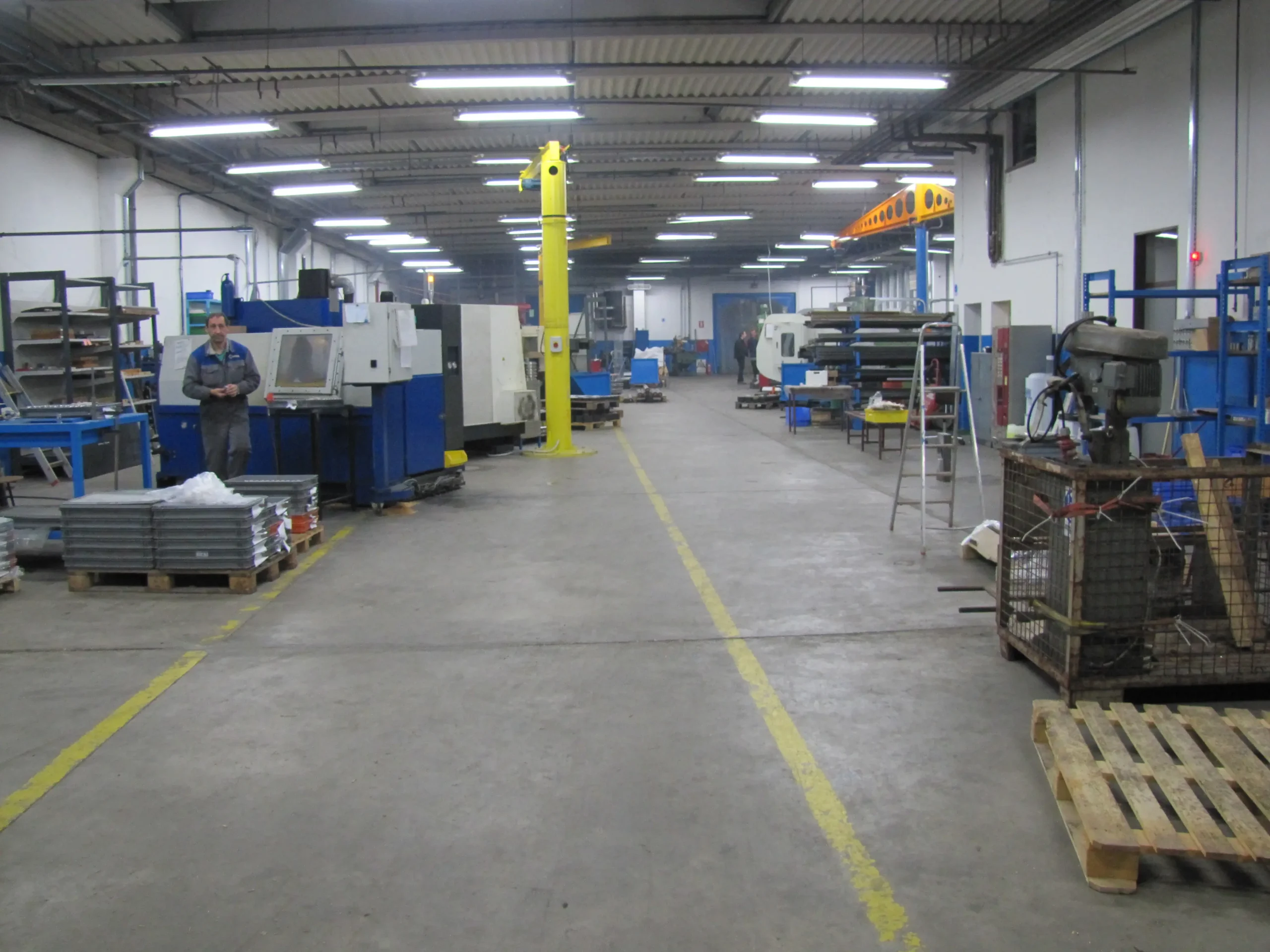 Pogled v proizvodno halo z delovnimi postajami, CNC stroji in delavcem pri delu