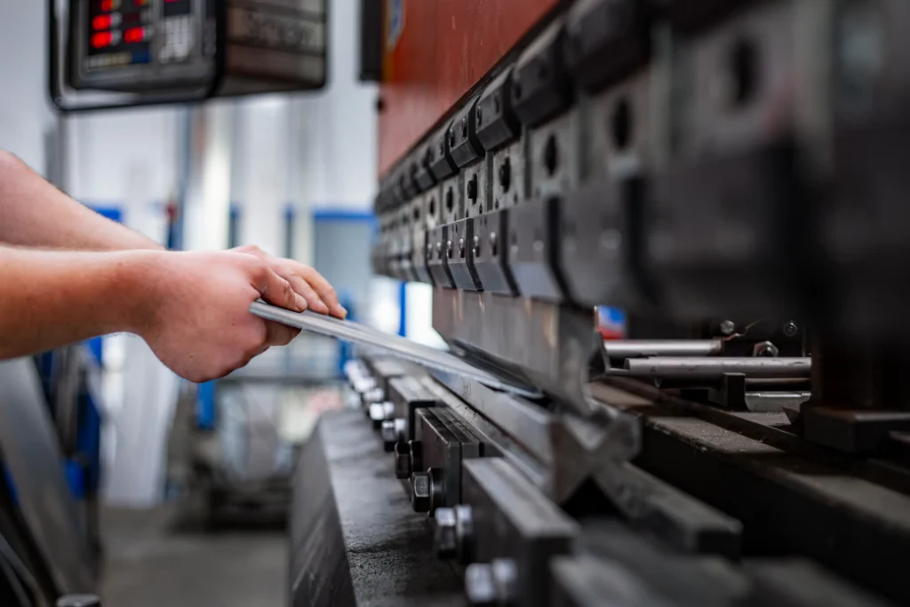 Roke delavca med postopkom krivljenja pločevine na hidravličnem stroju za upogibanje.