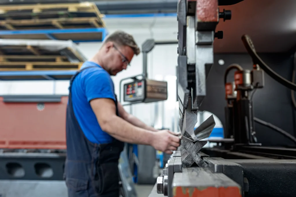 Delavec izvaja postopek krivljenja pločevine na stroju za preoblikovanje kovin v delavnici