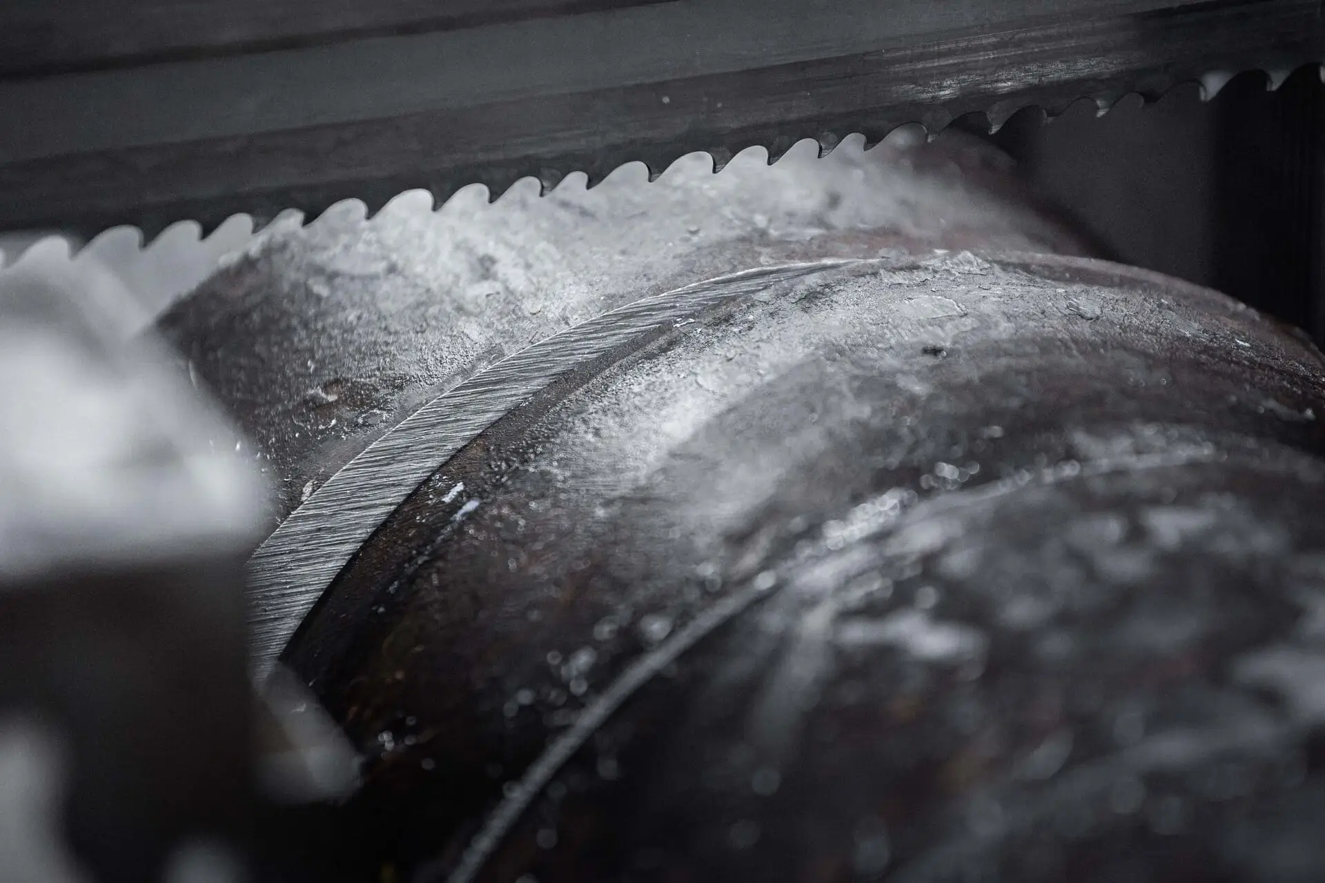 Zobato rezilo tračne žage med rezanjem velike kovinske cevi od blizu.