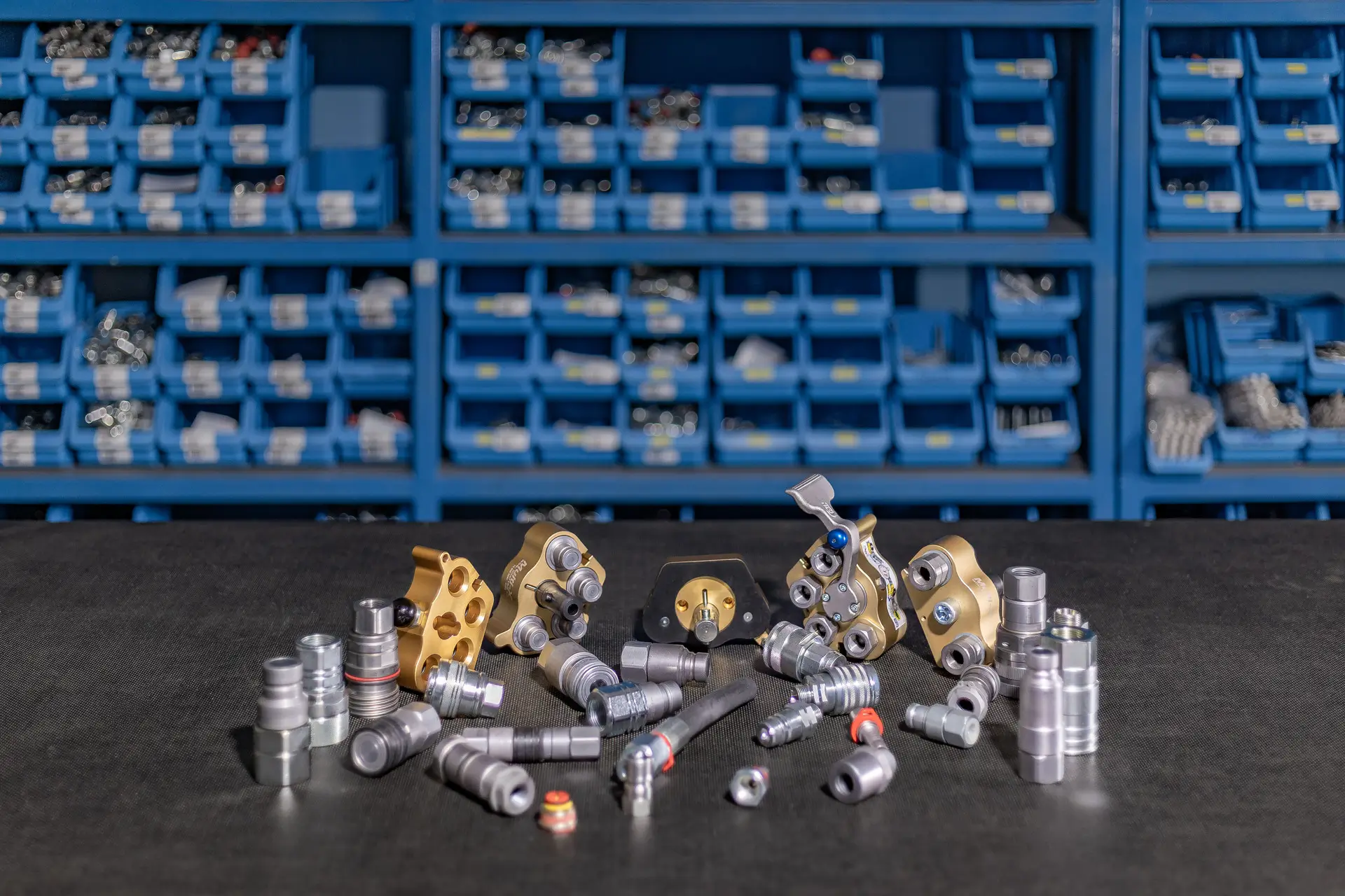 Hidravlične hitre spojke in ventili v zlatih in kovinskih odtenkih, razstavljeni na delovni površini.