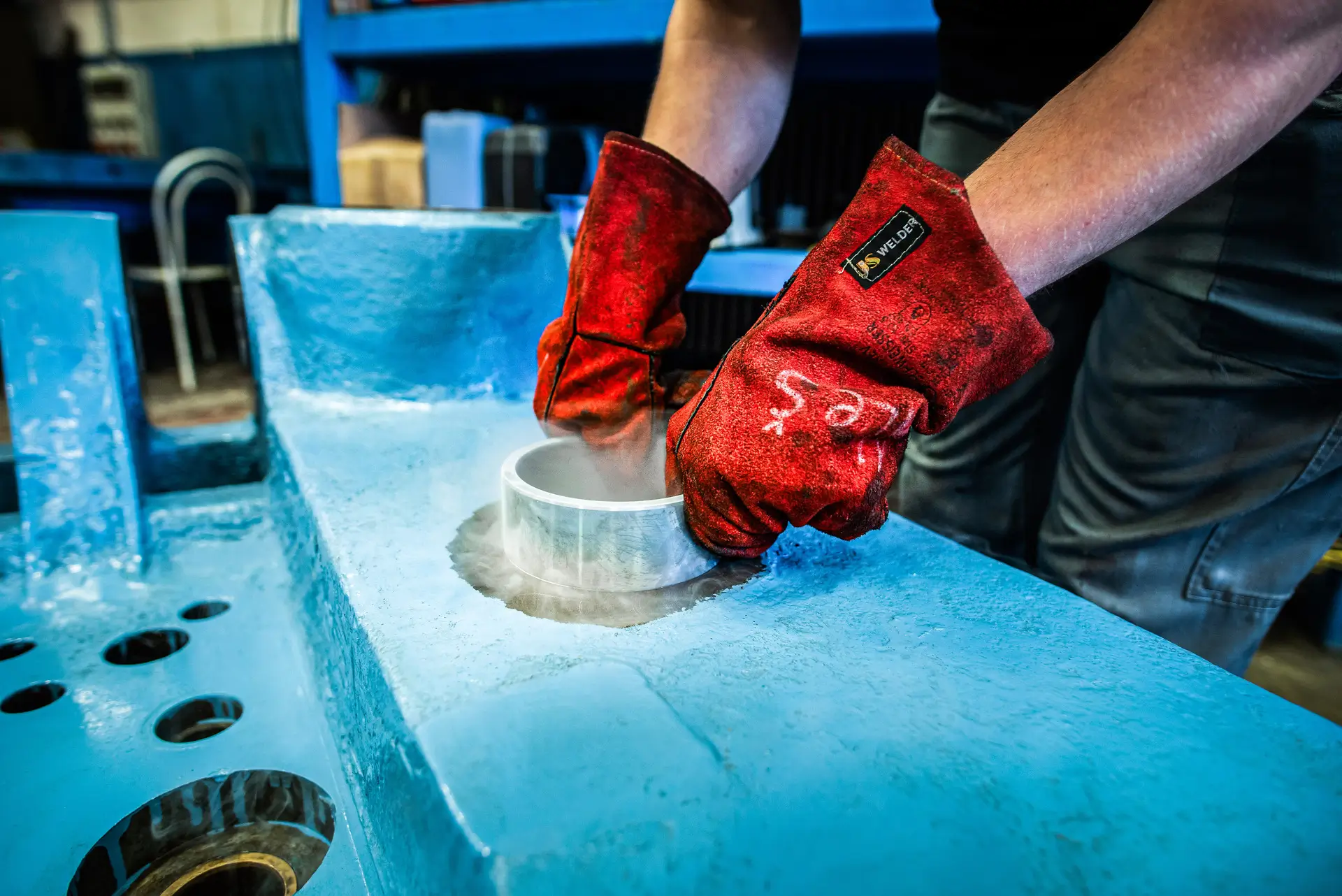 Delavec z rdečimi rokavicami vstavi ohlajeno pušo v ohišje orodja za tlačni liv aluminija.