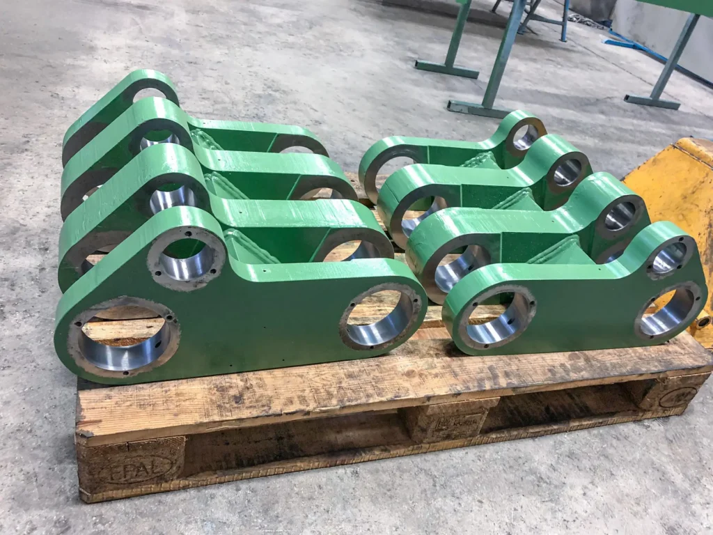 Zelene kovinske komponente po mehanski obdelavi pripravljene za montažo, postavljene na leseni paleti.